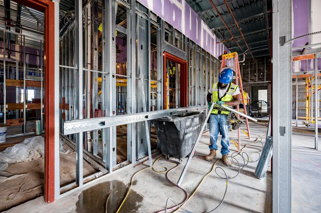 Worker on a ladder beside steel stud framing in an open building